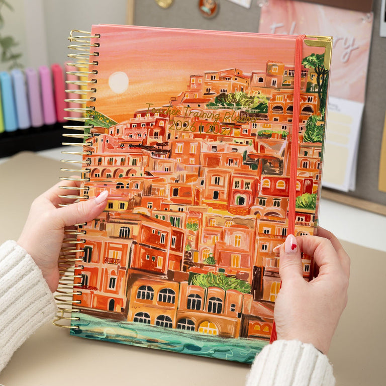 Person holding a spiral-bound notebook with a colorful cover of a cityscape.