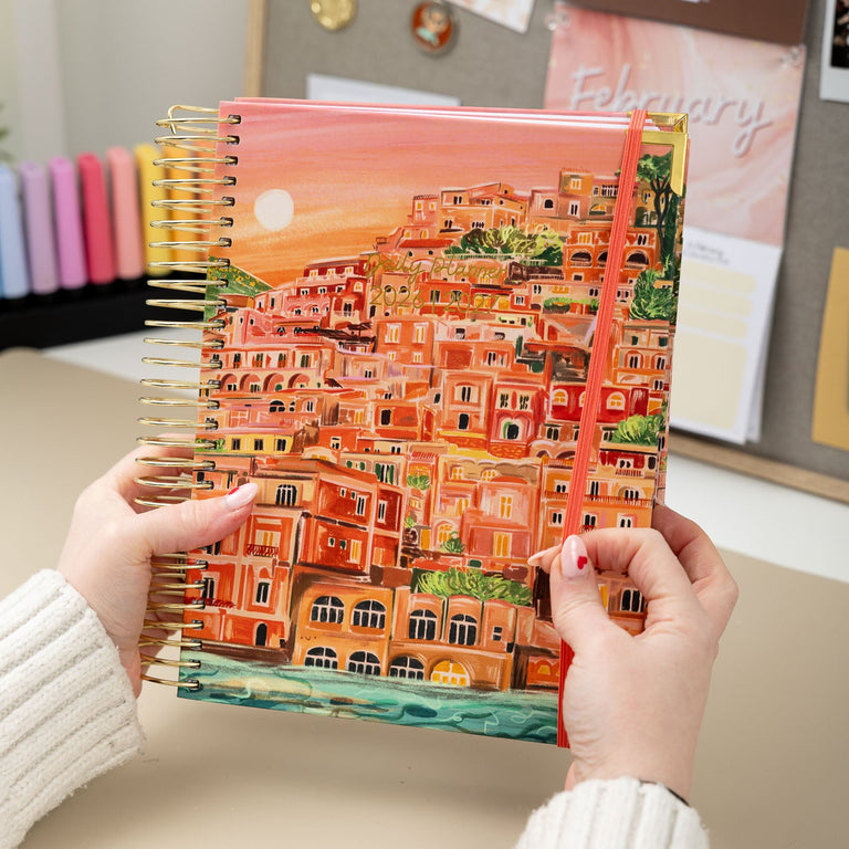 Person holding a colorful notebook with a scenic cover design.