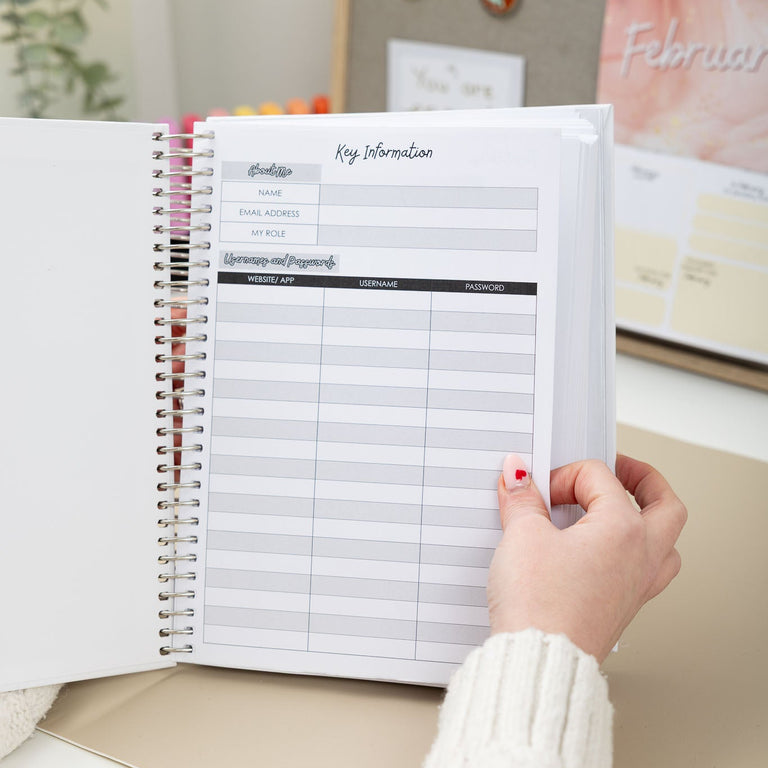 Person holding a planner with a calendar on a desk