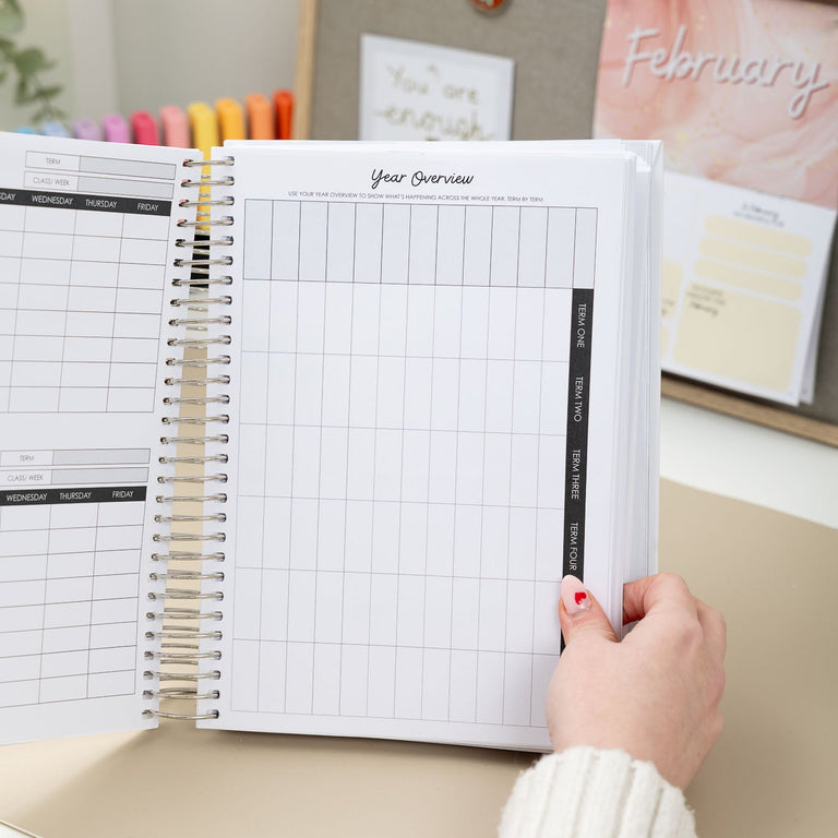 Person holding an open planner with a calendar on a desk