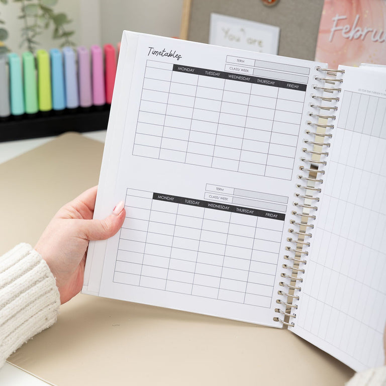 Person holding a spiral-bound planner with a calendar on a desk.