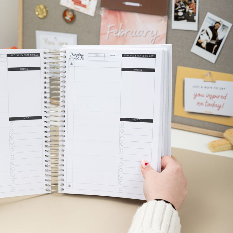 Person holding a planner with a calendar on a desk with photos and notes in the background