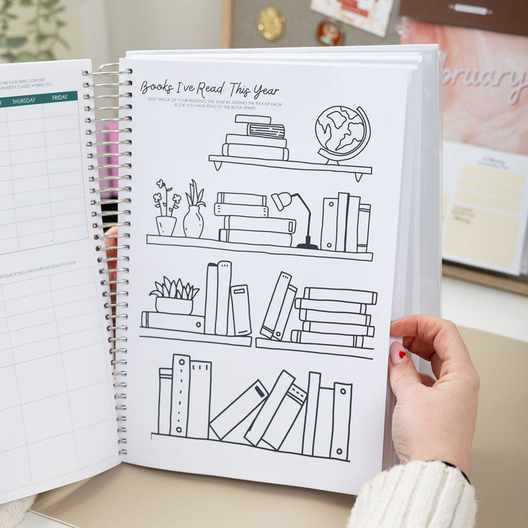 Person holding a spiral-bound notebook with a page of line art on a desk.