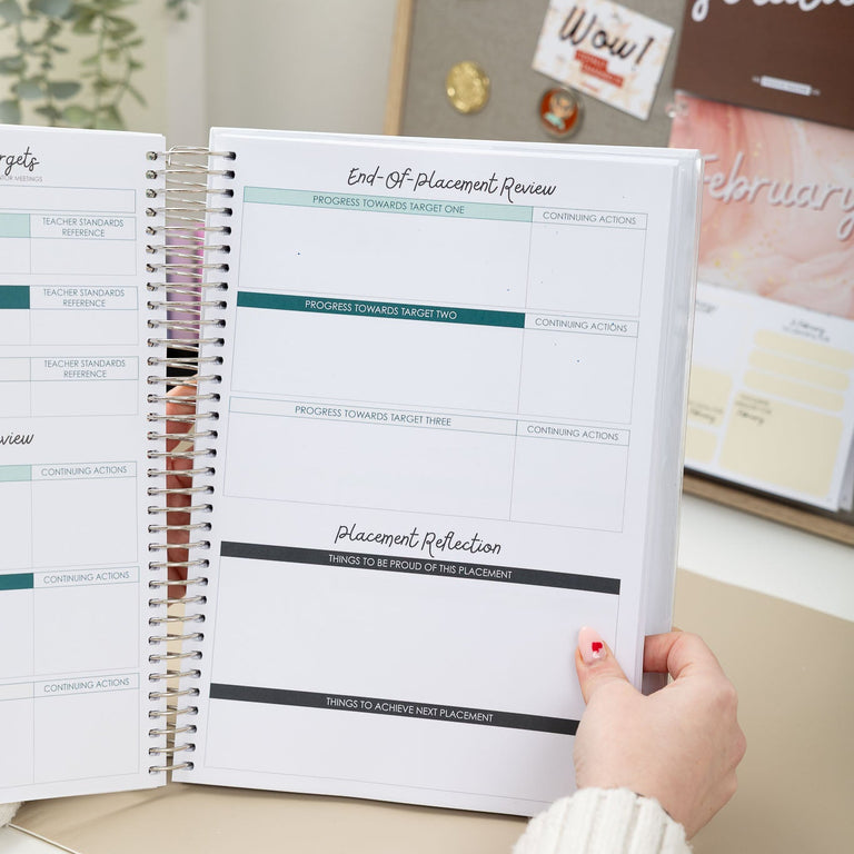 Person holding a spiral-bound planner with a focus on a page titled 'Placement Review'. The setting appears to be a desk with a bulletin board in the background.
