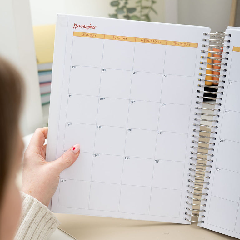Person holding a spiral-bound planner open to a calendar page.