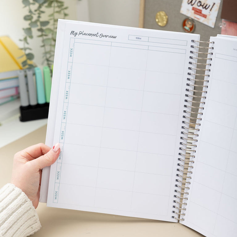 Person holding a spiral-bound planner with a calendar on a desk.