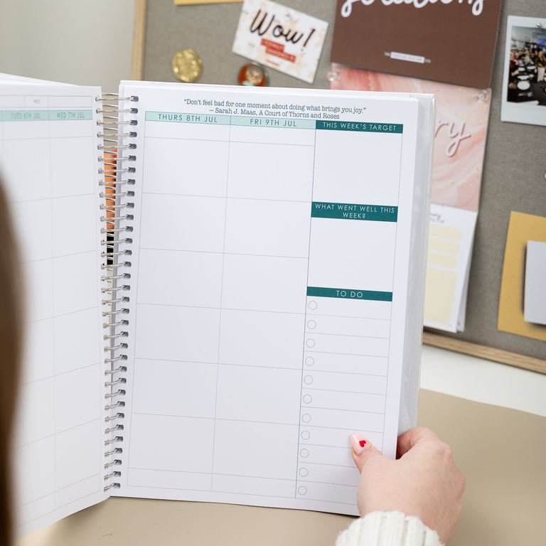 Person holding a spiral-bound planner with a colorful cover against a wall with motivational posters.