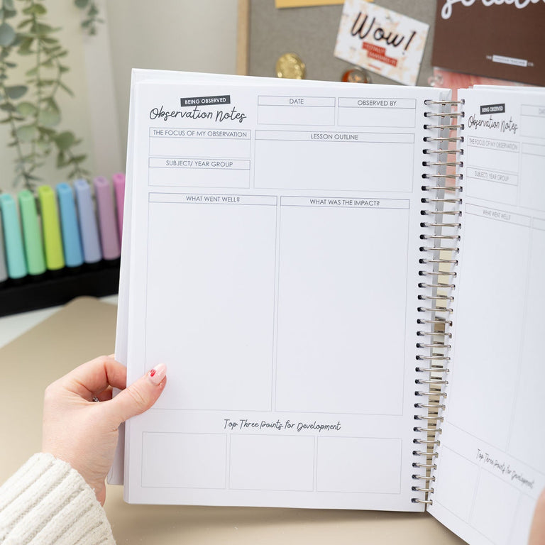 Person holding a spiral-bound planner with visible pages on a desk.