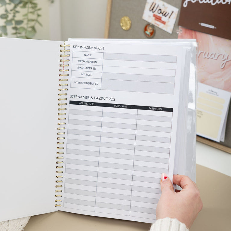 Person holding a spiral-bound planner with key information and contact details on a desk.