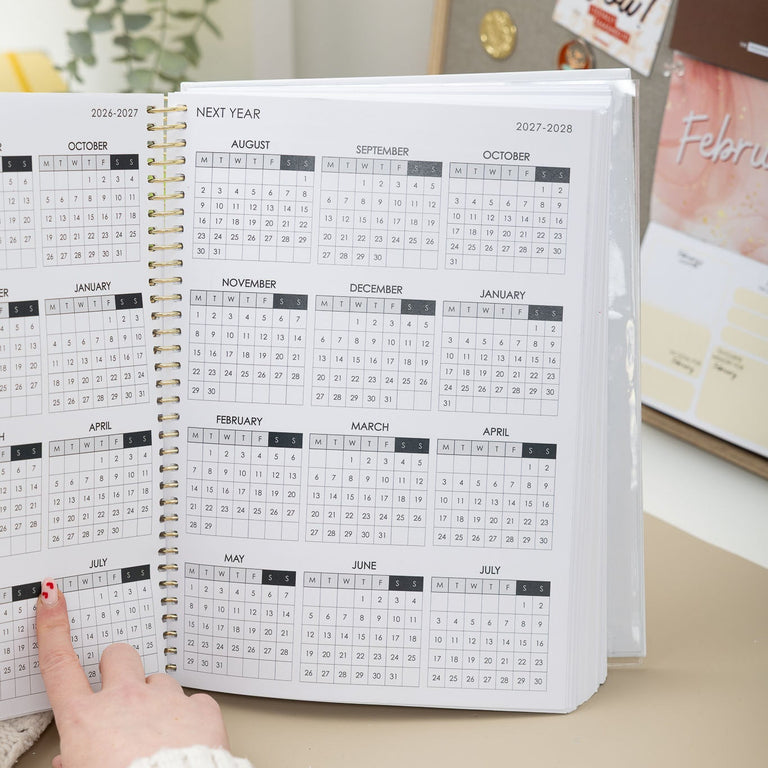 Person flipping through a large spiral-bound calendar on a desk.