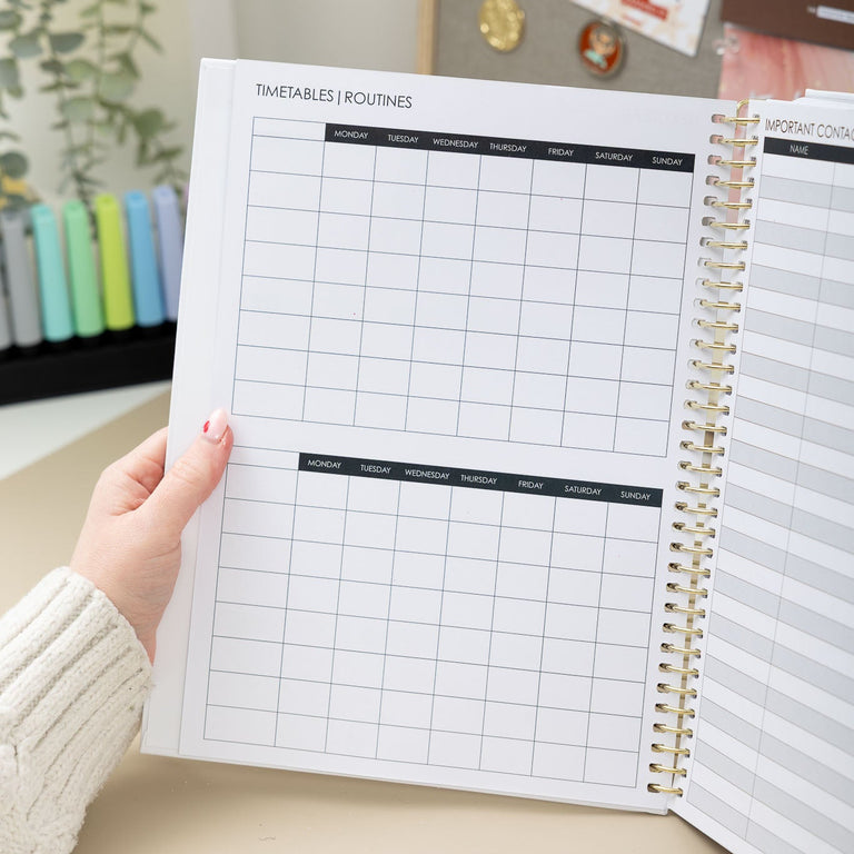 Person holding a spiral-bound planner with a grid layout on a desk.