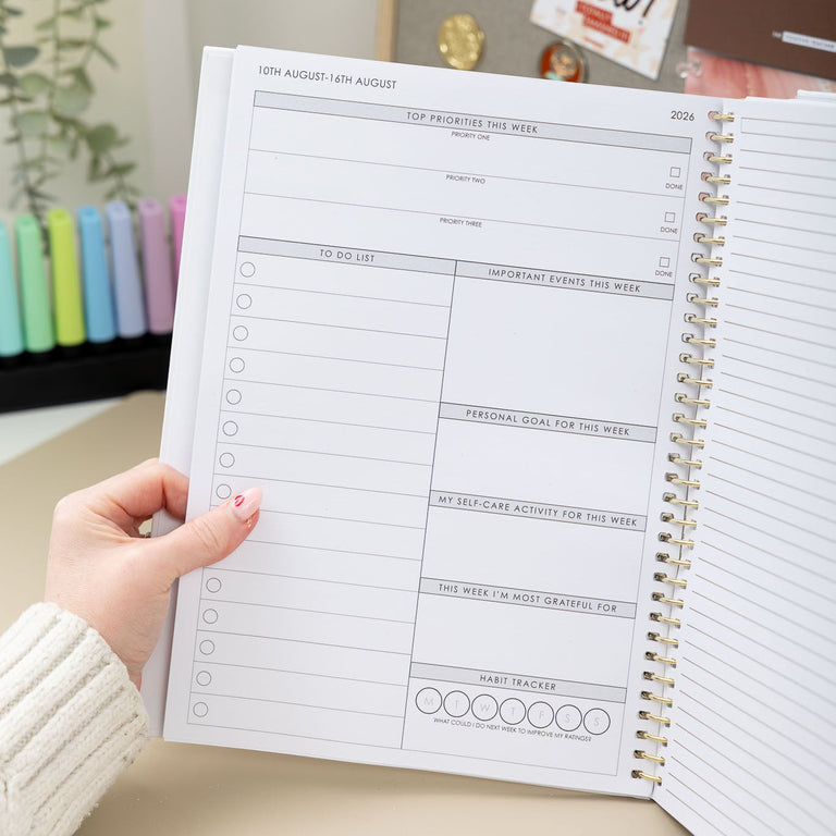 Person holding a spiral-bound planner with a visible layout on a desk.