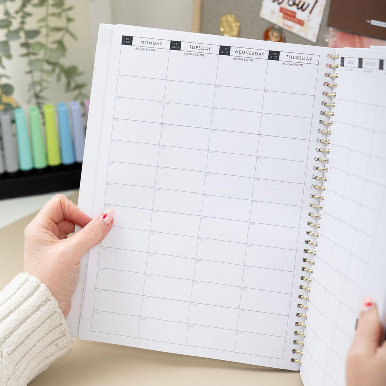Person holding a planner with a grid layout on a desk with decorative items in the background.