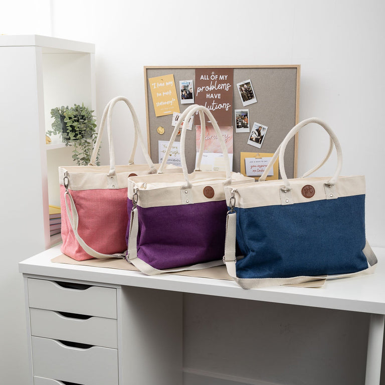 Three colorful bags on a desk with a white wall and bulletin board in the background