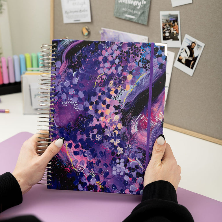 Person holding a colorful notebook with a bulletin board in the background