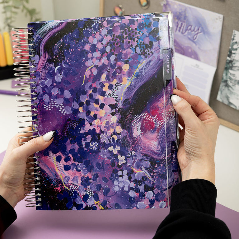 Person holding a colorful planner with a purple and pink design.