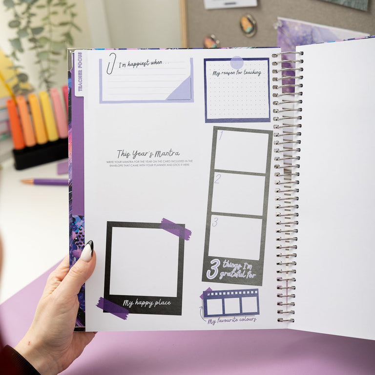 Person holding a spiral-bound planner with purple and white design on a desk.