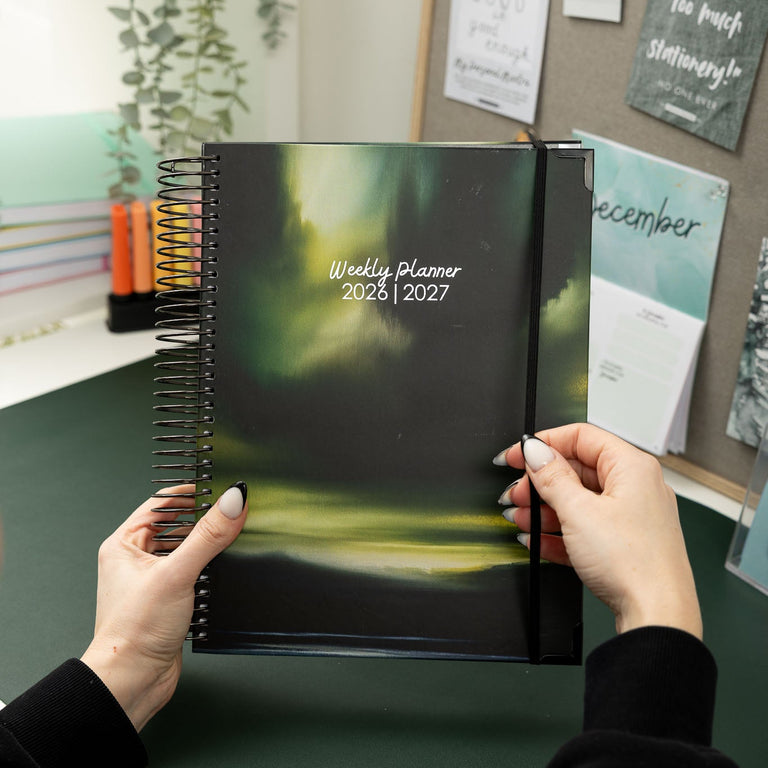 Person holding a weekly planner with a scenic cover in an office setting