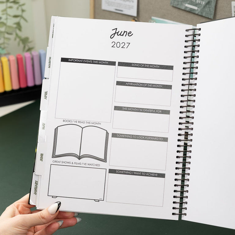 Person holding a planner with June 2023 layout on a desk with stationery items.