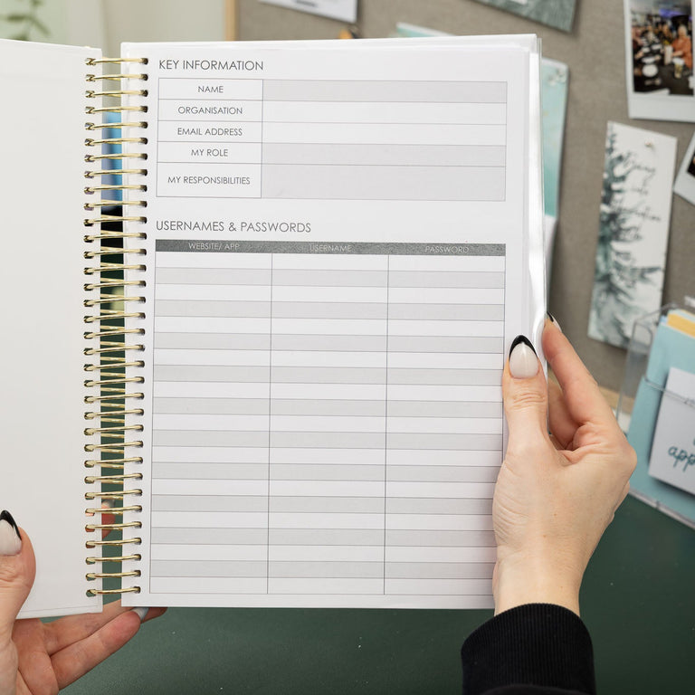 Person holding a spiral-bound planner with a grid layout on a desk.