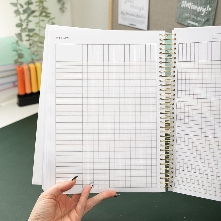 Person holding a spiral-bound notebook with grid paper on a desk.