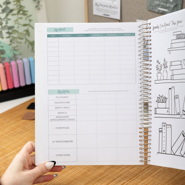 Open planner with a hand holding it on a wooden desk, with a blurred background