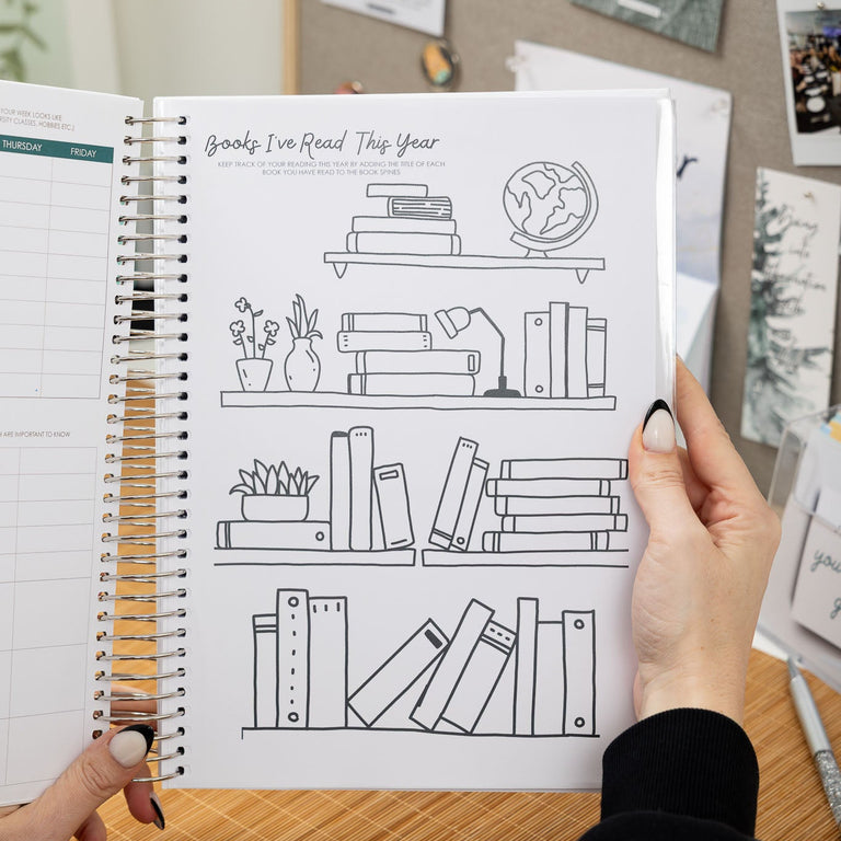 Person holding a spiral-bound notebook with a coloring page of a bookshelf.