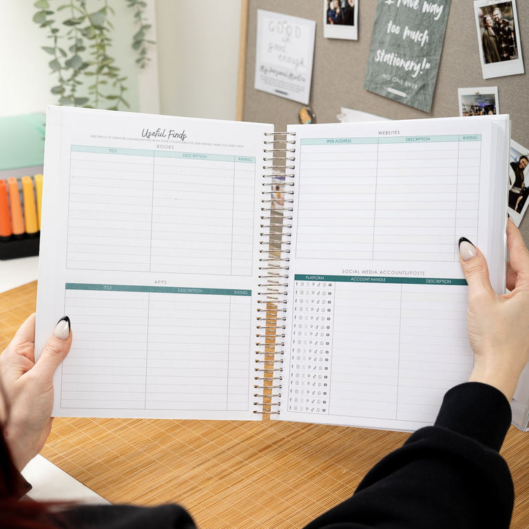 Person holding a planner open on a desk with a bulletin board in the background