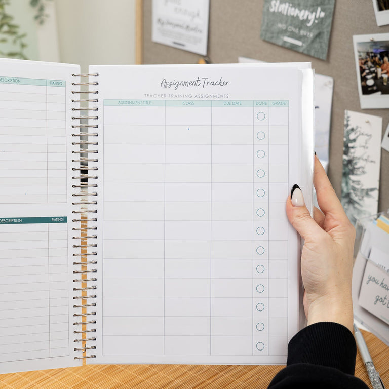 Person holding a spiral-bound planner with a hand on a desk, surrounded by photos and notes.