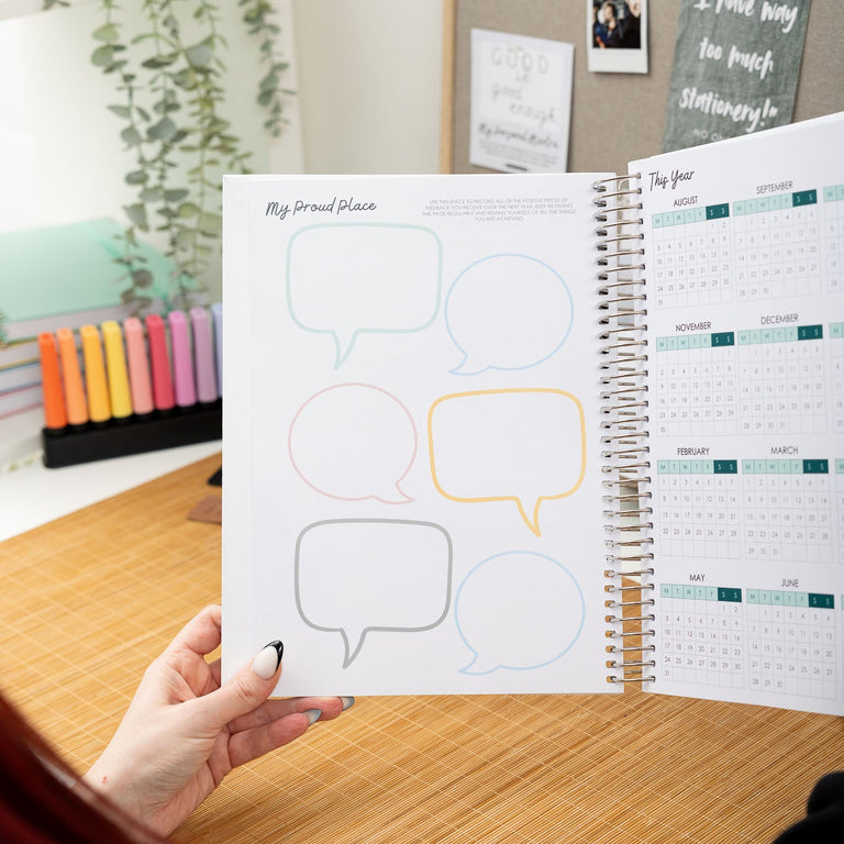 Person holding a planner with speech bubble designs on a desk with stationery items.