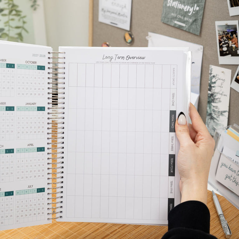 Person holding an open planner with a desk and wall with photos in the background