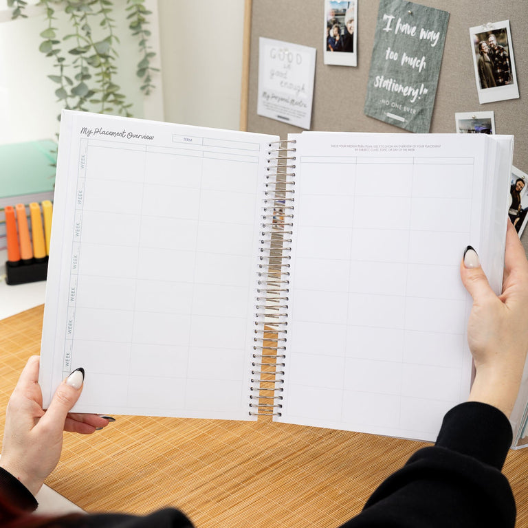 Person holding an open planner with a desk and bulletin board in the background