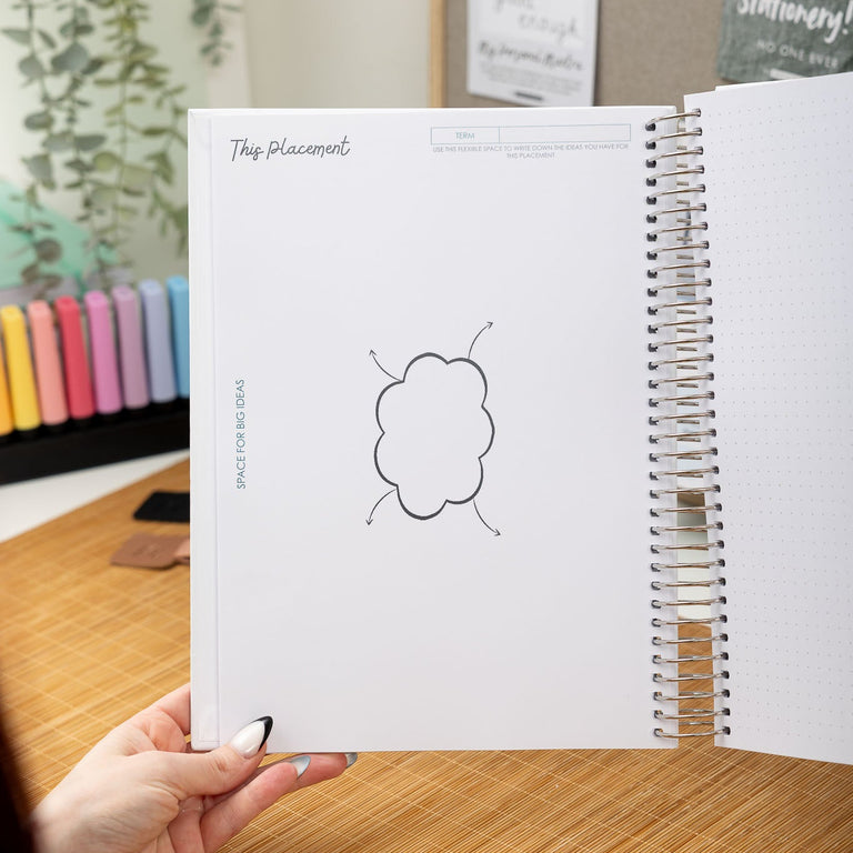 Person holding a spiral-bound notebook with a cloud illustration on a desk.