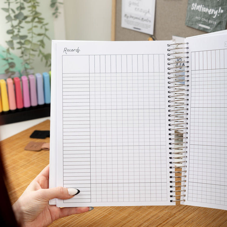 Person holding a spiral-bound notebook with grid pages on a desk.