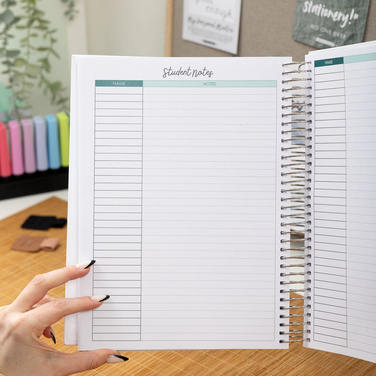 Person holding a spiral-bound notebook with lined pages on a wooden desk.