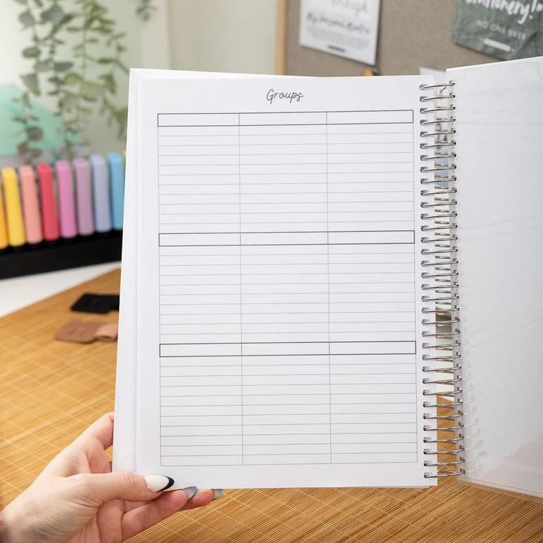 Person holding a spiral-bound notebook with lined pages on a wooden desk.