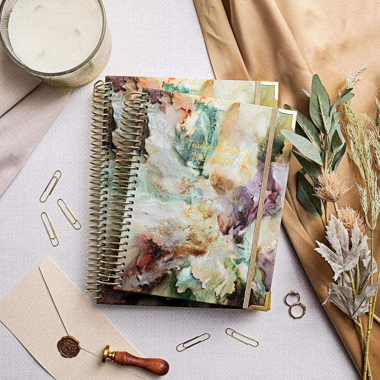 Decorative planner with floral design on a table with a candle, paper clips, and dried plants.