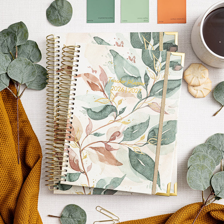 Notebook with floral design, coffee cup, and eucalyptus leaves on a white surface