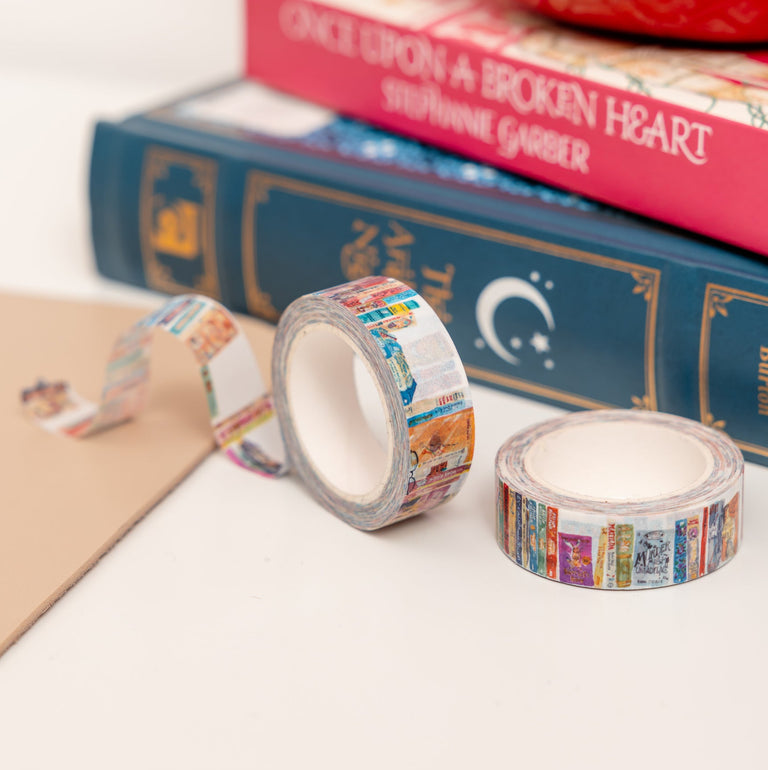Two rolls of decorative tape with book-themed designs on a white surface, with books and a red mug in the background.