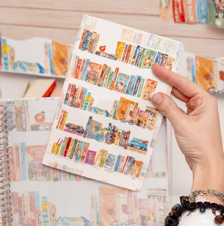 Person holding a colorful planner with stationery items on a desk