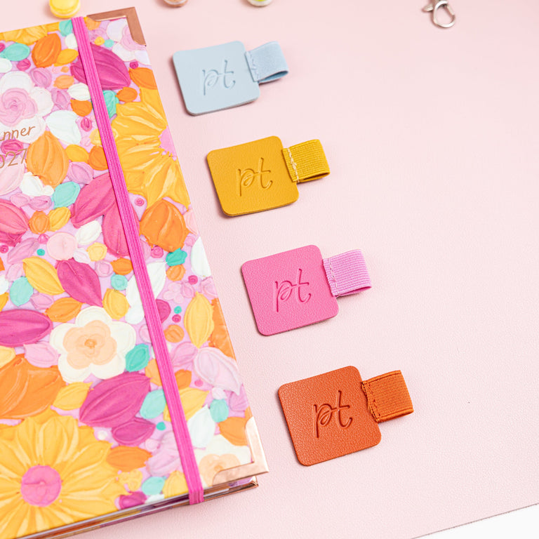 Colorful planner with floral design, stickers, and a lanyard on a pink background