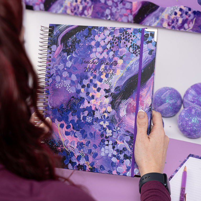 Person holding a purple planner with artistic design on a matching desk