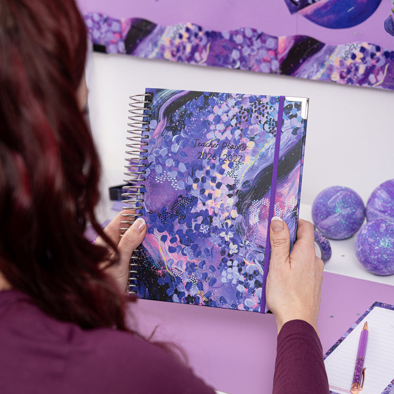 Person holding a spiral-bound notebook with a purple and blue abstract design on a desk.