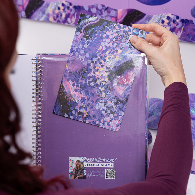 Person holding a purple notebook with a colorful design on a purple background