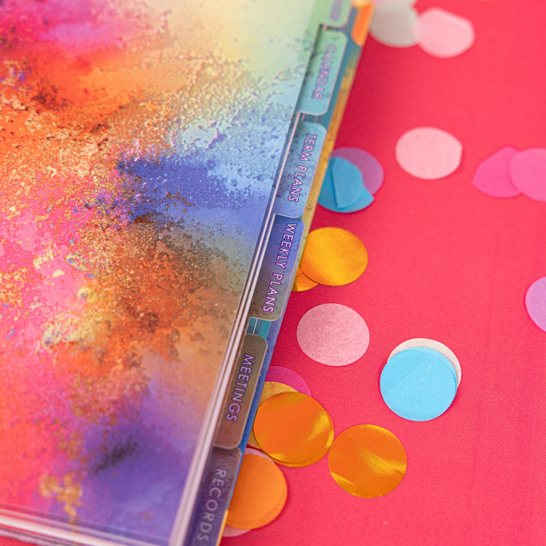Colorful book with glittery cover on a pink background with confetti