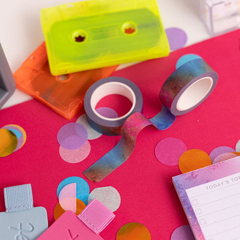 Colorful cassette tapes, washi tape, and decorative items on a pink surface with confetti.