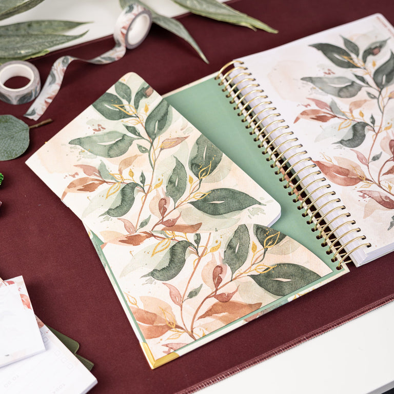 Open spiral-bound notebook with floral design on a maroon surface with green leaves.