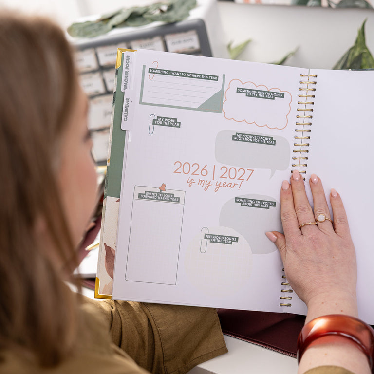 Person holding a planner with 2026-2027 layout, sitting in a floral chair.