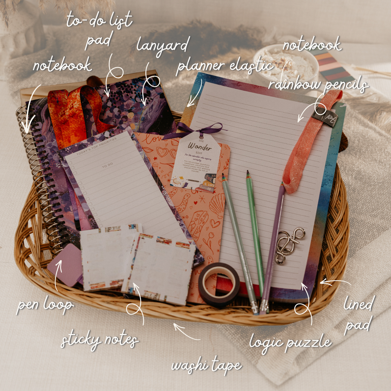 A styled flat-lay of a stationery bundle arranged in a wicker basket, including notebooks, a planner elastic, rainbow pencils, sticky notes, washi tape, a logic puzzle pad, and a to-do list pad, with handwritten callouts pointing to each item.